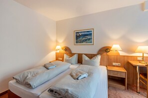 Hotellihuone, jossa on kaksi sänkyä, yöpöytä, työpöytä ja taulu seinällä.