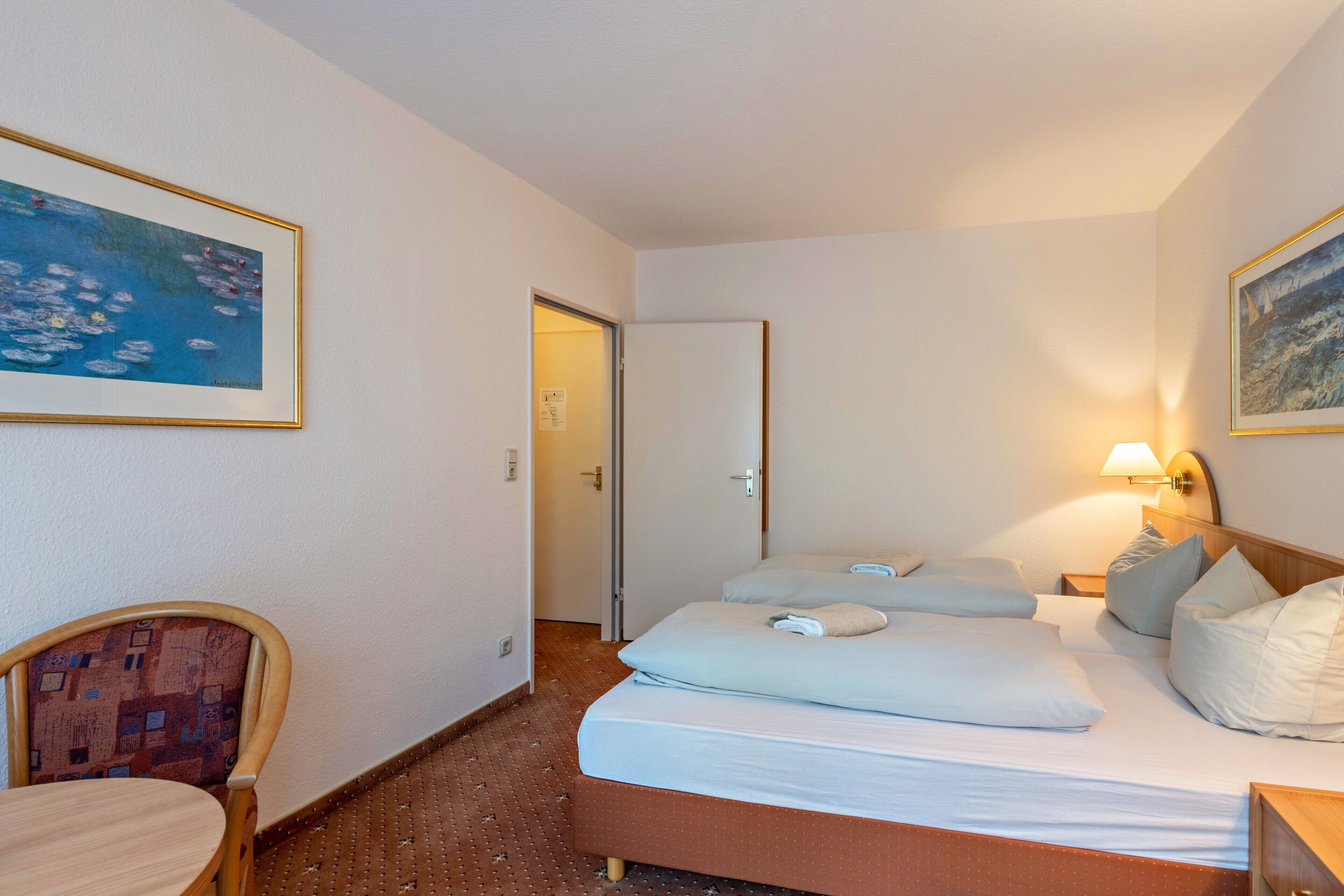 Un cuarto de hotel con una cama, una silla, una mesa y dos cuadros en las paredes.