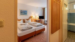 Habitación de hotel con cama, escritorio, silla, televisión y baño visible a través de una puerta abierta.