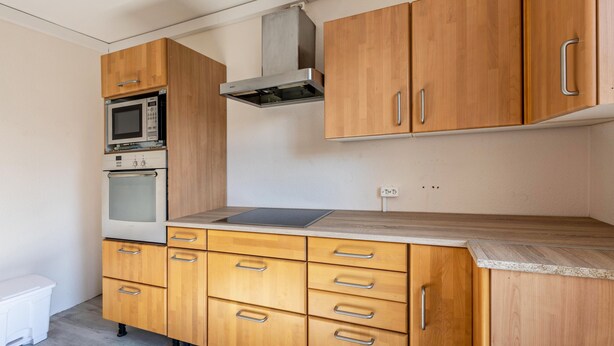 Una cocina con armarios de madera, microondas, horno y una campana extractora de acero inoxidable.