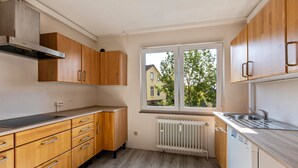 Una cocina con armarios de madera, una campana extractora de acero inoxidable, una ventana con vistas a una casa y un lavavajillas empotrado.