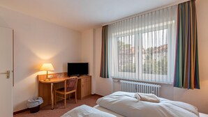Une chambre d’hôtel avec un lit, un bureau avec une télévision, une chaise et une fenêtre avec des rideaux.