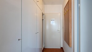 Un couloir étroit aux murs blancs, une porte en bois et un sol à motifs marron.