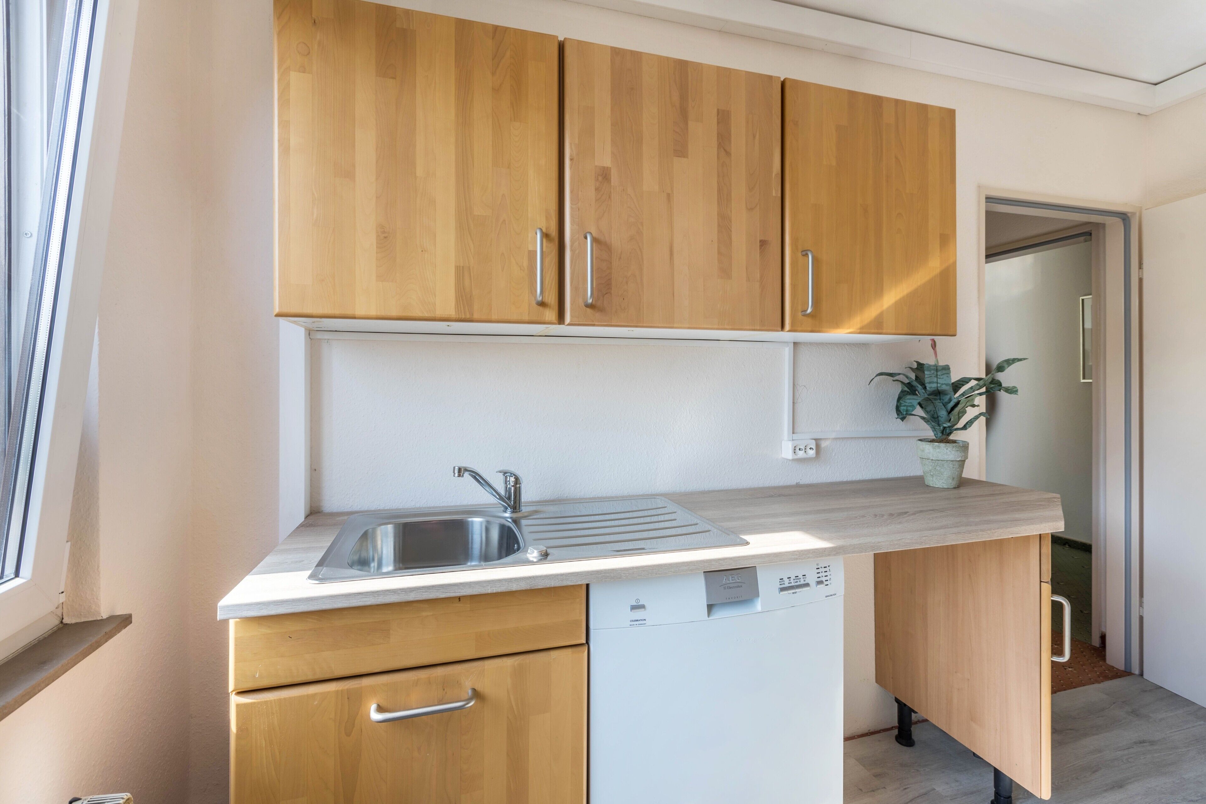 Una cocina compacta con armarios de madera, lavavajillas integrado y una ventana.