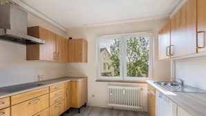 Eine Küche mit Holzausstattung, einer Edelstahl-Spüle und einem Fenster mit Blick auf ein Haus.