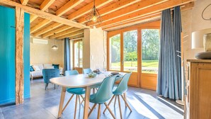 A modern interior with a dining area, wooden beams, large windows, and a view of greenery. - Gîte Le Pigeonnier with Shared Pool, Wi-Fi, and Air Conditioning (Chassaignes)
