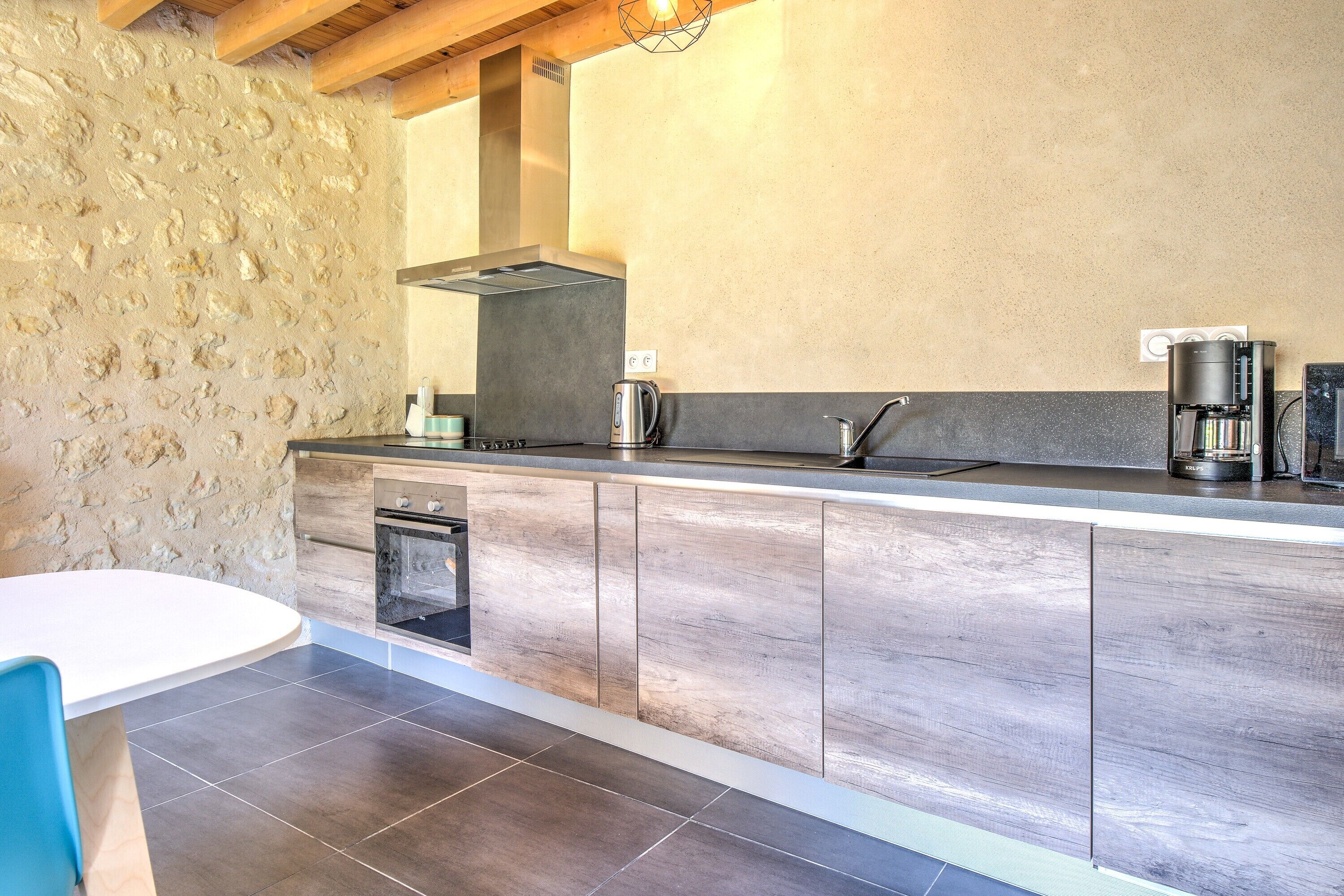 Una cocina moderna con pared de piedra, armarios de madera, horno empotrado y una mesa redonda.