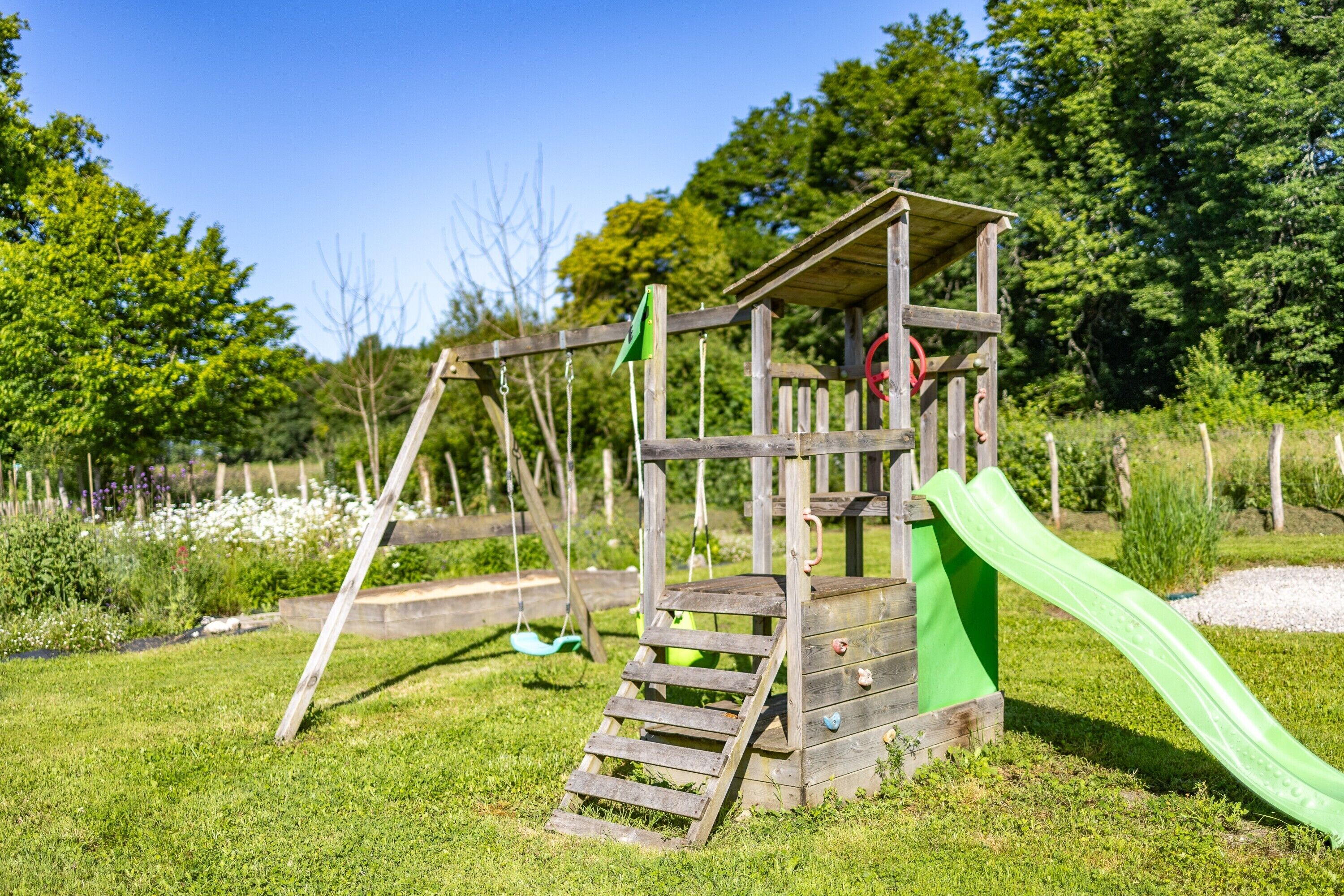 A wooden play structure with a slide and swings in a grassy area.