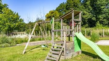 A wooden play structure with a slide and swings in a grassy area.