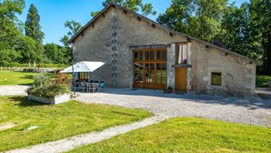 Un bâtiment en pierre avec une allée gravillonnée, un espace extérieur aménagé avec des sièges et une grande fenêtre.