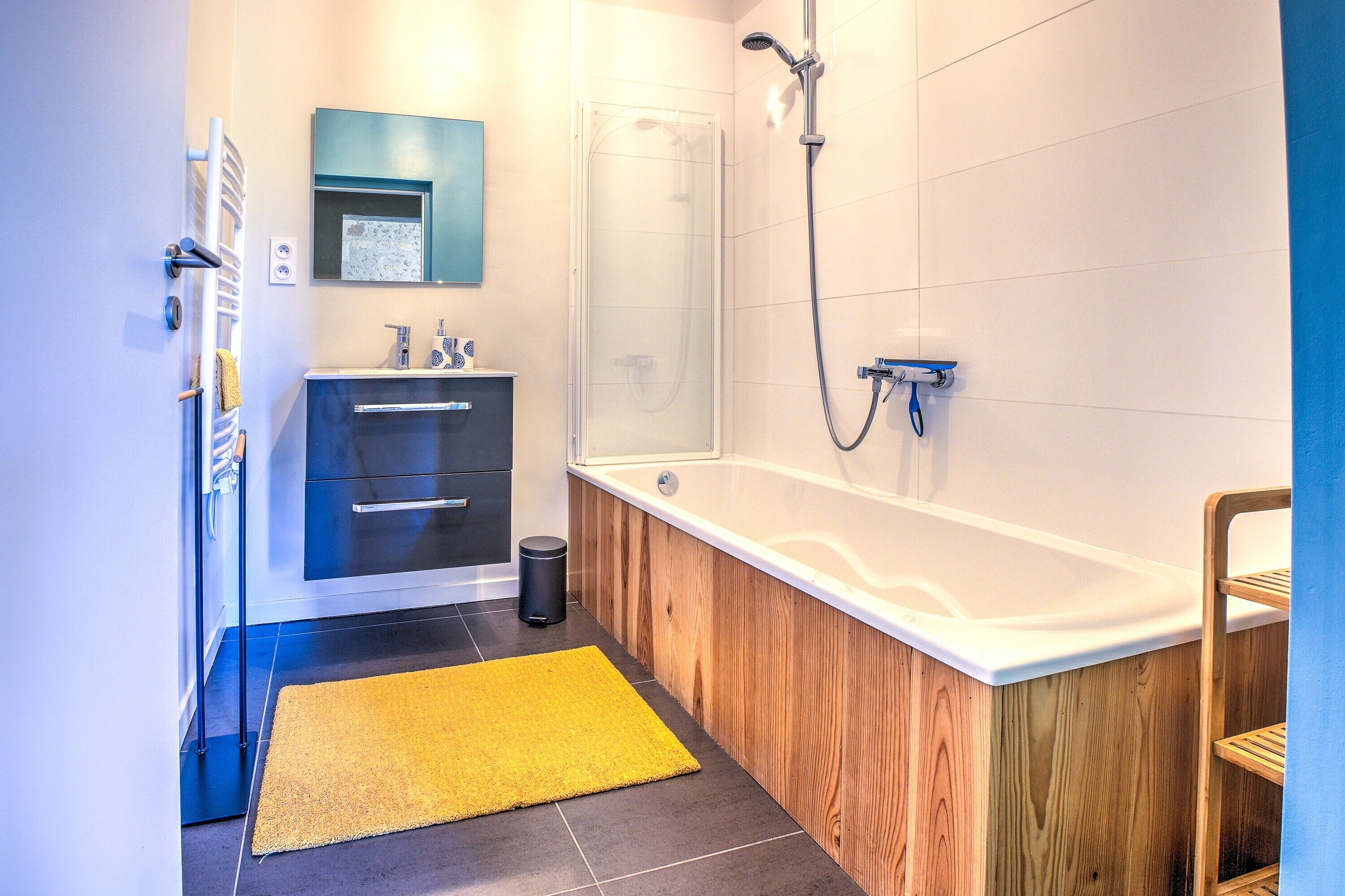 Une salle de bain moderne avec un meuble-lavabo en bois, une baignoire, une douche et un tapis jaune.