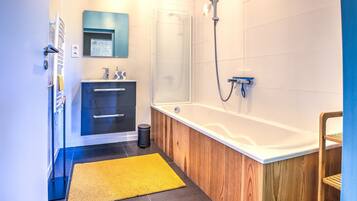 Une salle de bain moderne avec un meuble-lavabo en bois, une baignoire, une douche et un tapis jaune.