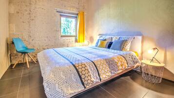 A bedroom with a bed, a chair, a window with curtains, and a bedside lamp.