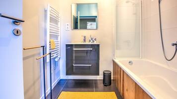 A modern bathroom with a bathtub, a shower, a sink with a mirror, and a towel rack.