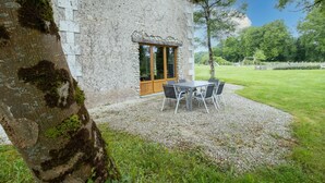 Un edificio de piedra con puerta de madera, un patio de grava y una mesa con sillas.