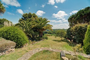 Un jardín con un camino de piedra, diversos árboles y un cielo despejado.