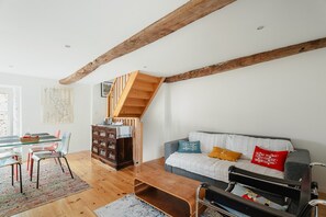Una sala de estar con una escalera de madera, un sofá con cojines, una mesa de comedor con sillas y un aparador de madera.