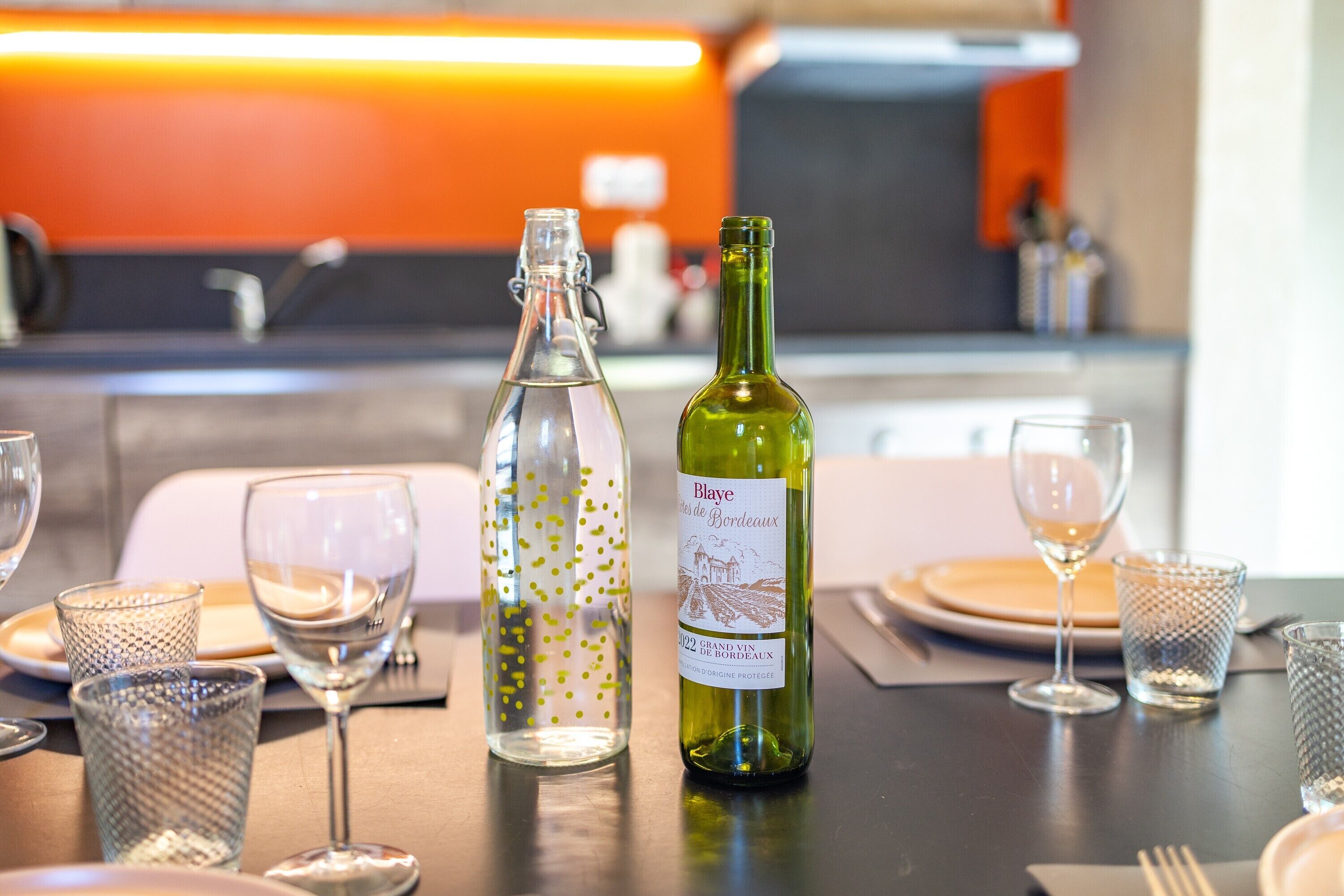 Una mesa dispuesta con copas de vino, una botella y un recipiente de vidrio decorativo.