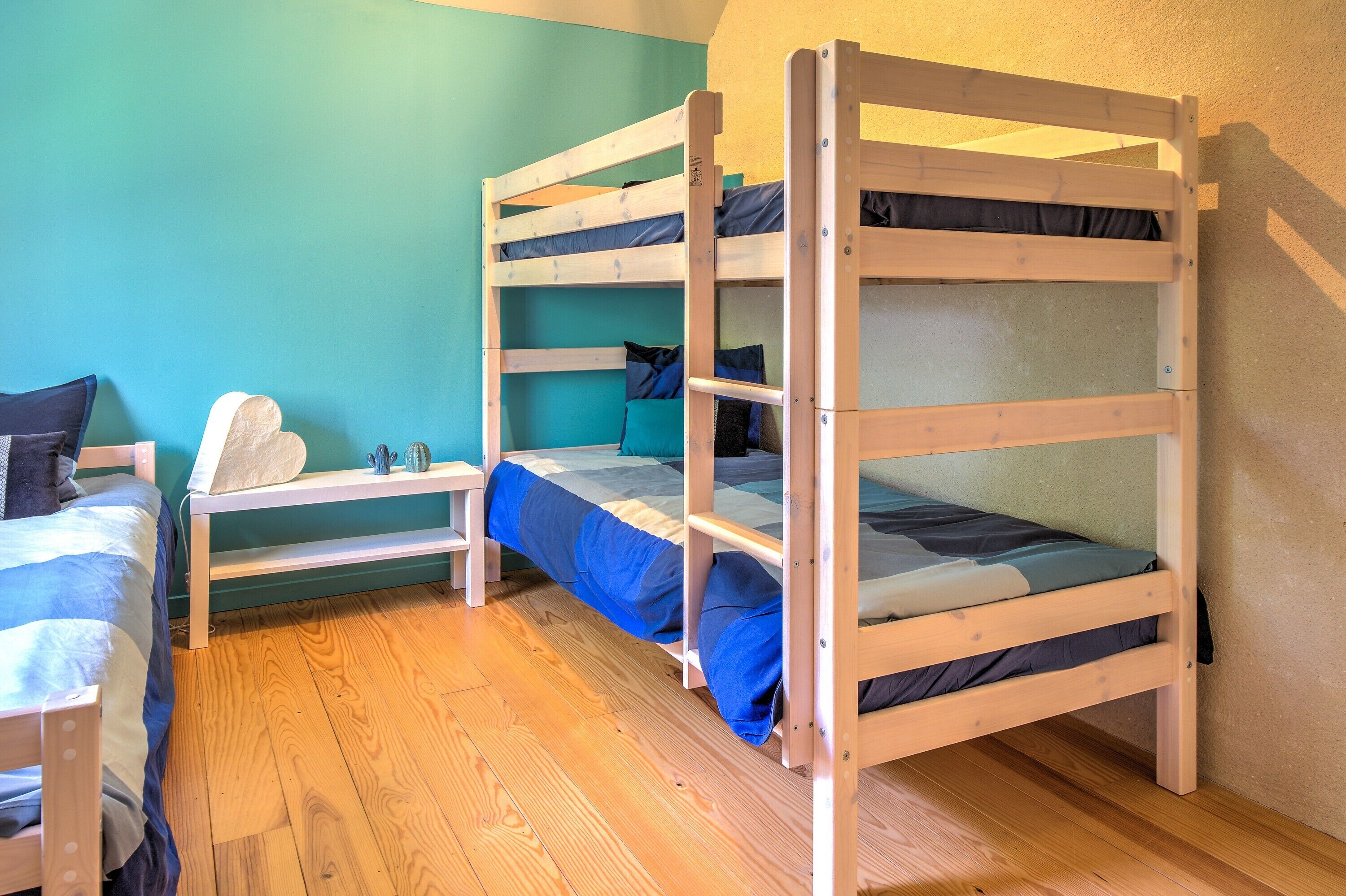 A bunk bed room with a wooden floor, teal walls, and a small table with a pillow.