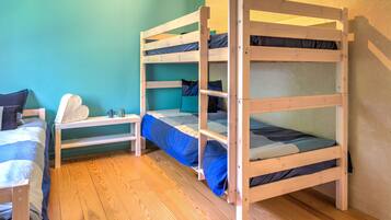 A bunk bed room with a wooden floor, teal walls, and a small table with a pillow.