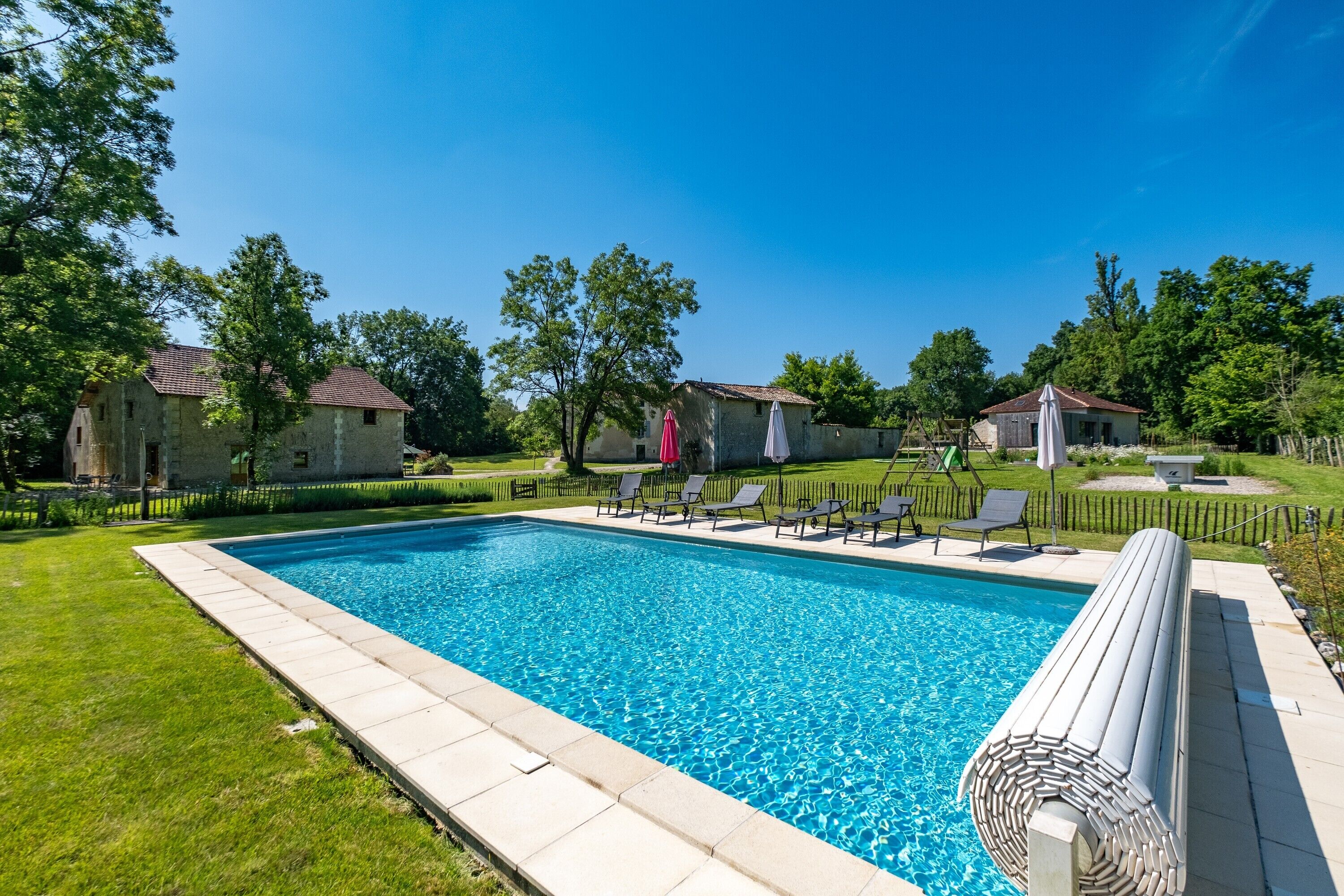 Une piscine rectangulaire à l’eau d’un bleu limpide, entourée d’une pelouse bien entretenue et de quelques arbres.