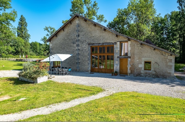 A stone building with a gravel driveway, a covered outdoor seating area, and a large window.