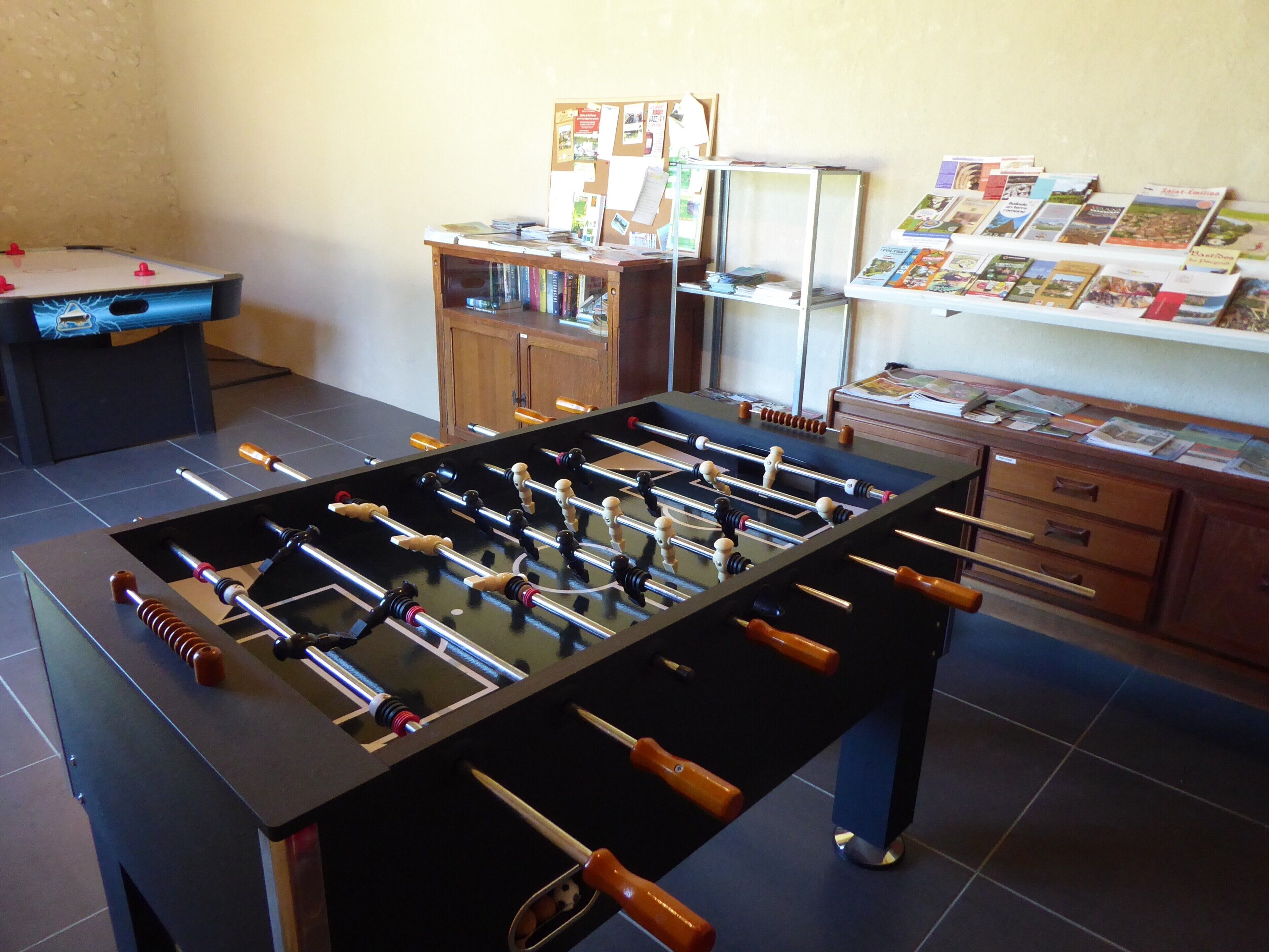 A room with a foosball table, a bookshelf, and a desk with papers.