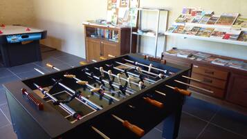 A room with a foosball table, a bookshelf, and a desk with papers.