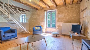 Una habitación rústica con una escalera de madera, un televisor, un sofá y una pequeña mesa.