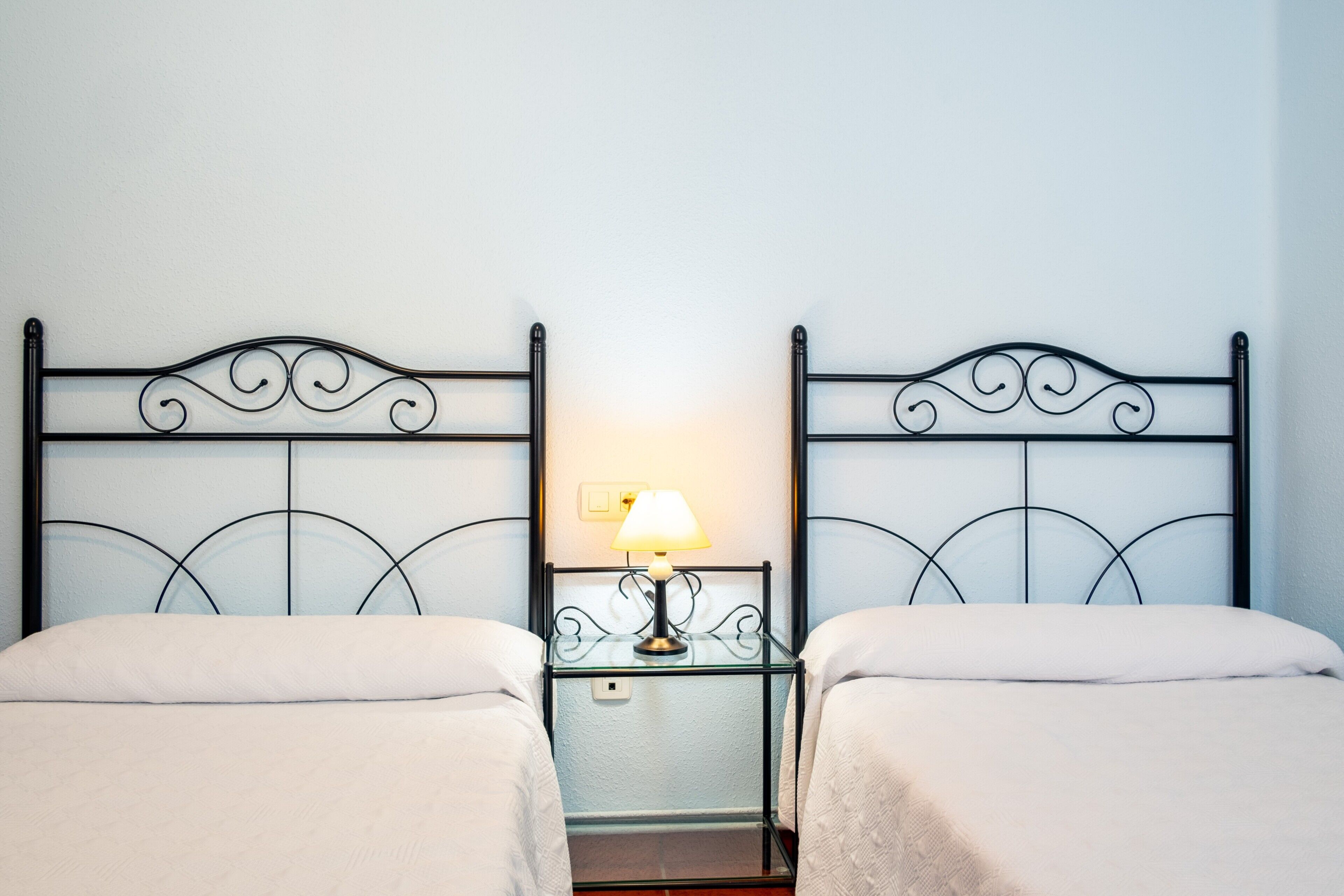 Habitación doble con dos camas, una mesita de noche con lámpara y un espejo.