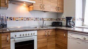 A kitchen with wooden cabinets, a white stove, a dishwasher, a coffee maker, and a toaster. - Holiday Home 'El Parral' with Mountain Views, Shared Terrace and Wi-Fi (La Rinconada de la Sierra)