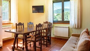 A dining area with a table and chairs, a television on the wall, a window with curtains, and a radiator. - Holiday Home 'El Parral' with Mountain Views, Shared Terrace and Wi-Fi (La Rinconada de la Sierra)