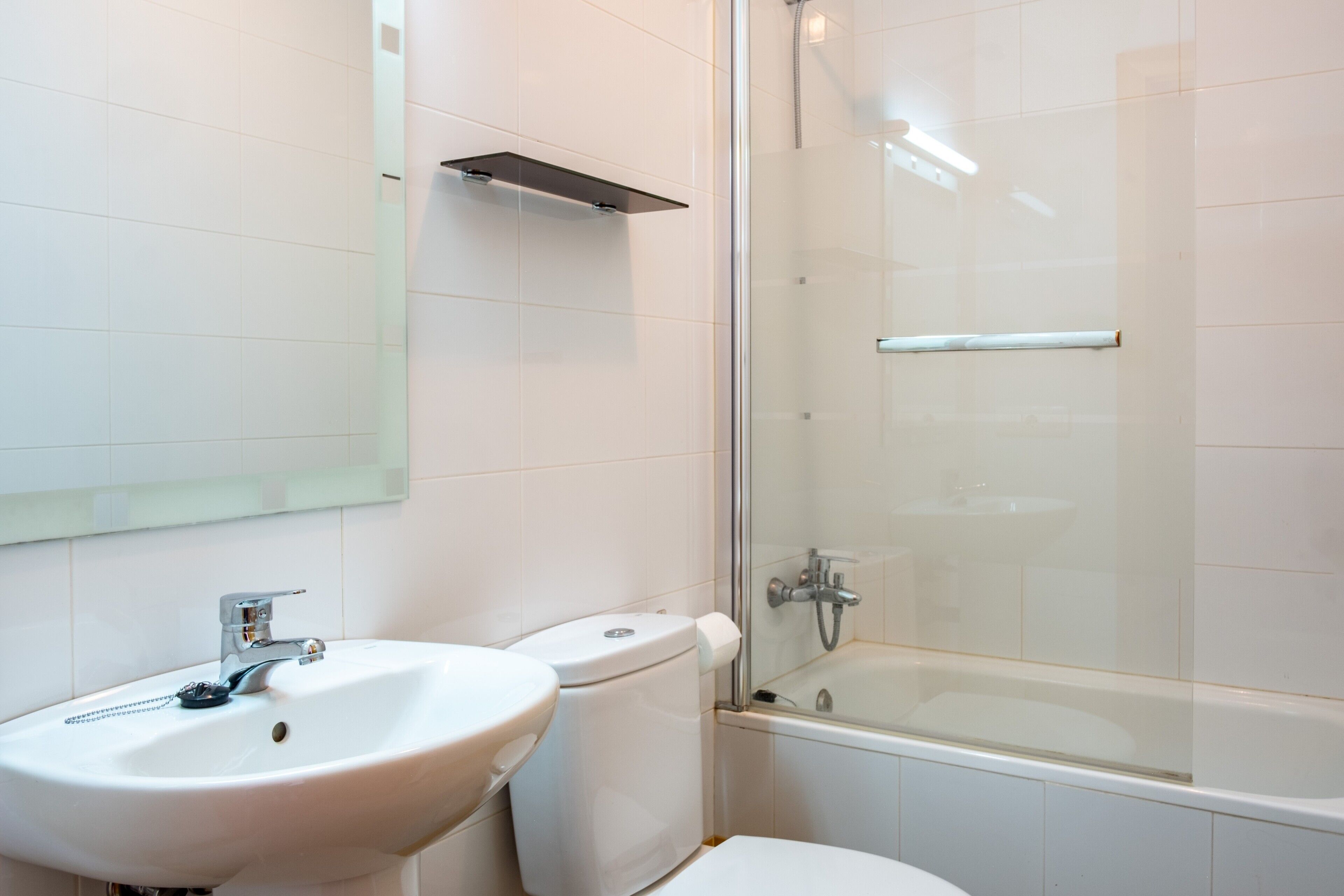 Un baño con lavamanos, inodoro y ducha con mampara de vidrio.
