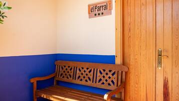 Eine hölzerne Bank vor einer Wand in Blau-Weiß gehalten, eine Tür mit Messinggriffen und ein Schild mit der Aufschrift 'elParral'.