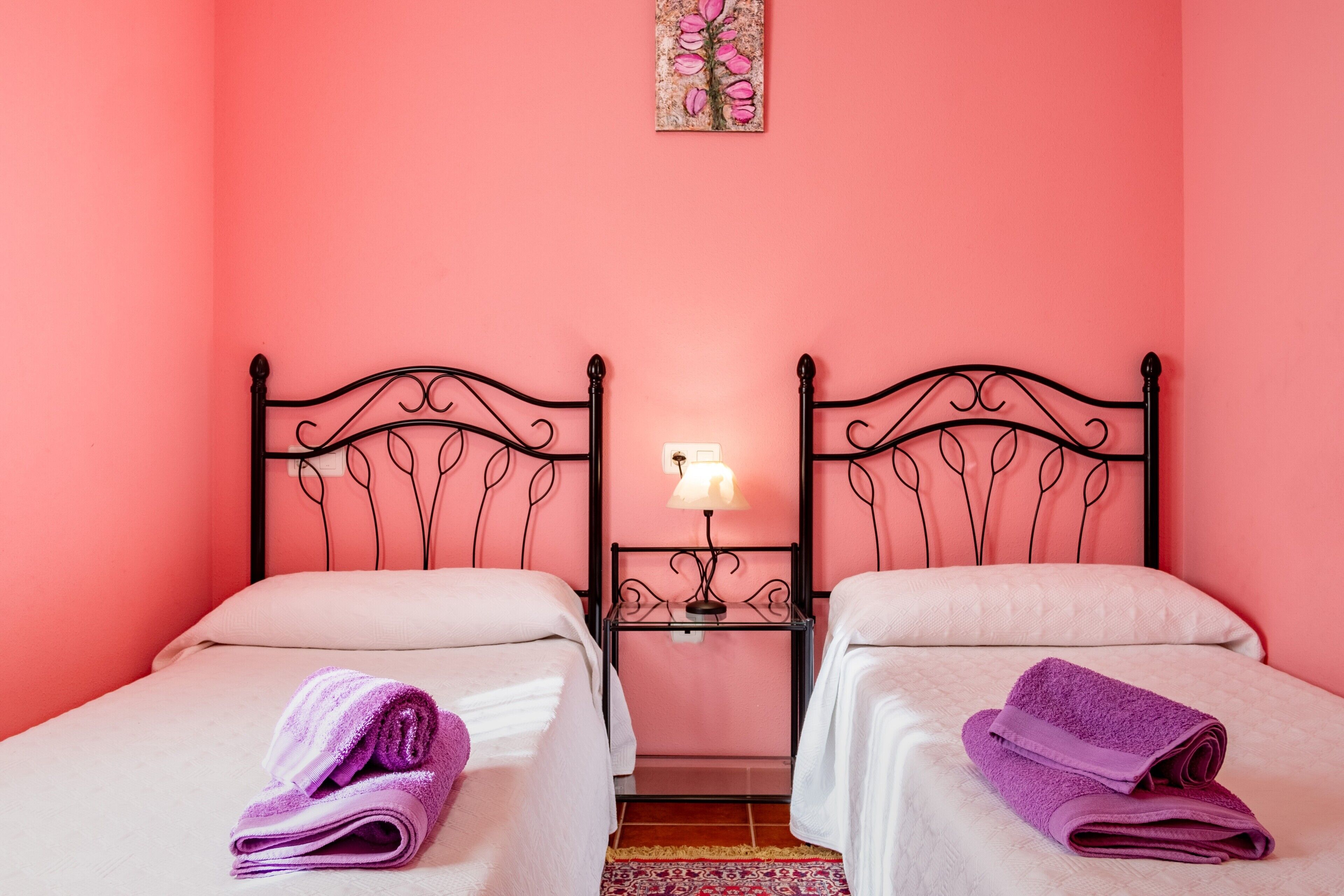 Une chambre avec deux lits, une table de chevet avec une lampe et une œuvre d’art aux motifs floraux accrochée au mur.