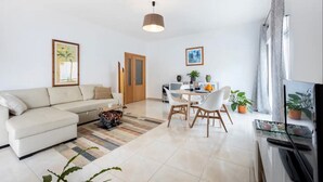 Ein modernes Wohnzimmer mit einer Couch, einem Esstisch, Stühlen, einem Fernseher und einem großen Fenster.