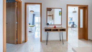 Ein modernes Interieur mit Holzboden, einem zentralen Spiegel, einem kleinen Tisch mit einem roten Gegenstand und Blick in einen anderen Raum mit Essbereich.