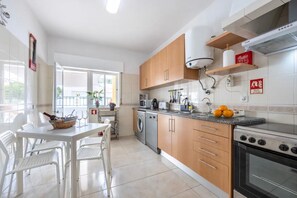 A modern kitchen with wooden cabinets, a built-in oven, and a dining area with white chairs and a table. - Apartment 'Casa Cláudia - Centro Histórico' with Private Terrace, Balcony and Wi-Fi (Lagos)