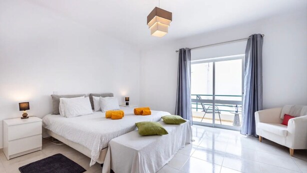 Ein modernes Schlafzimmer mit Bett, Nachttischen, Schreibtisch, Stuhl und Balkonblick.