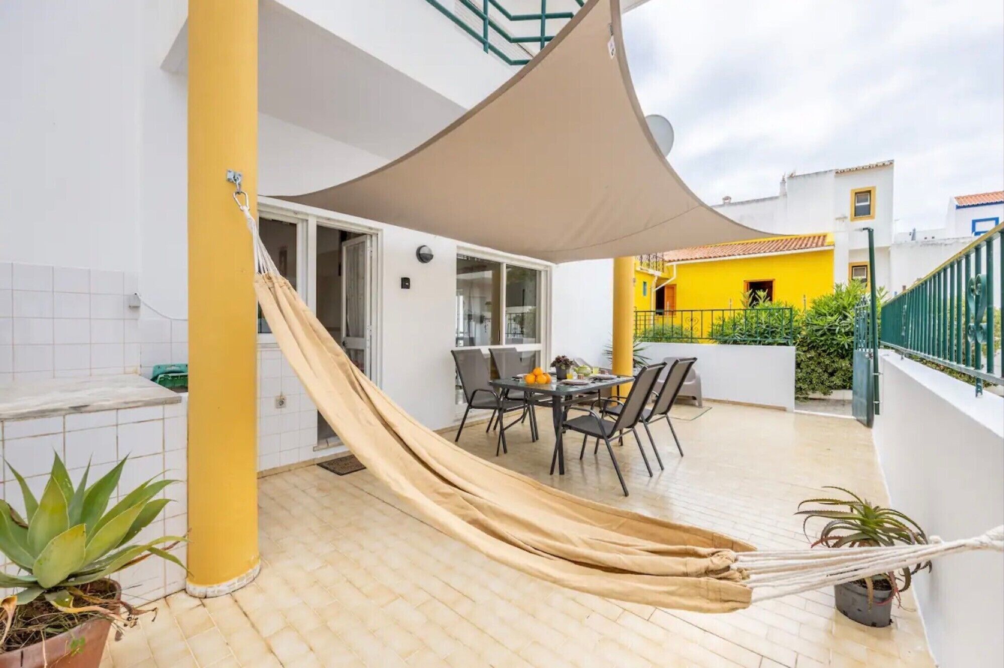 Une terrasse avec un hamac, une table à manger, des chaises et un mur jaune en arrière-plan.