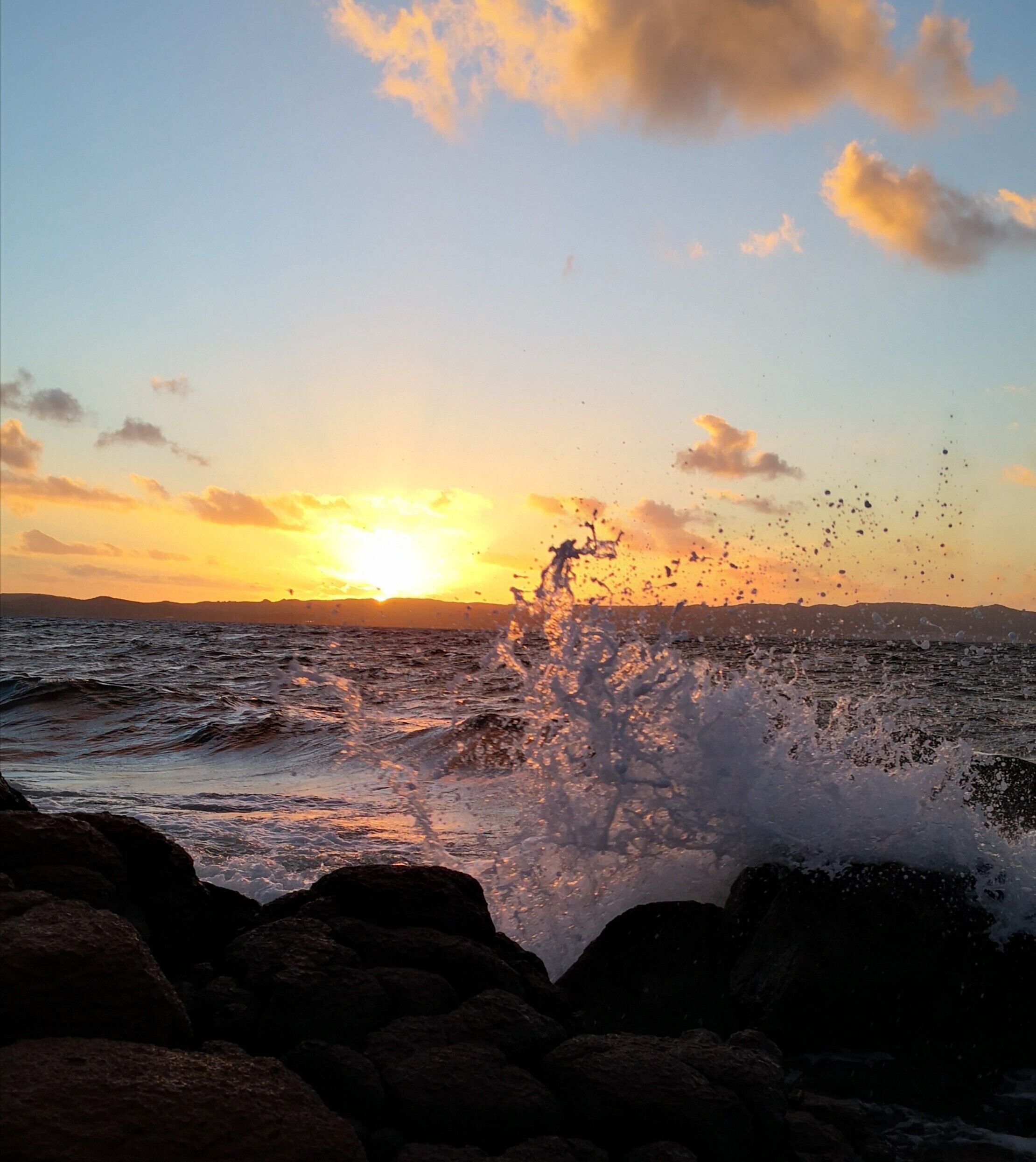 Un atardecer sobre una costa rocosa con olas rompiendo contra las rocas.
