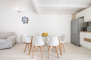 Una cocina moderna con armarios blancos, un refrigerador de acero inoxidable y un comedor con mesa de vidrio y sillas blancas.