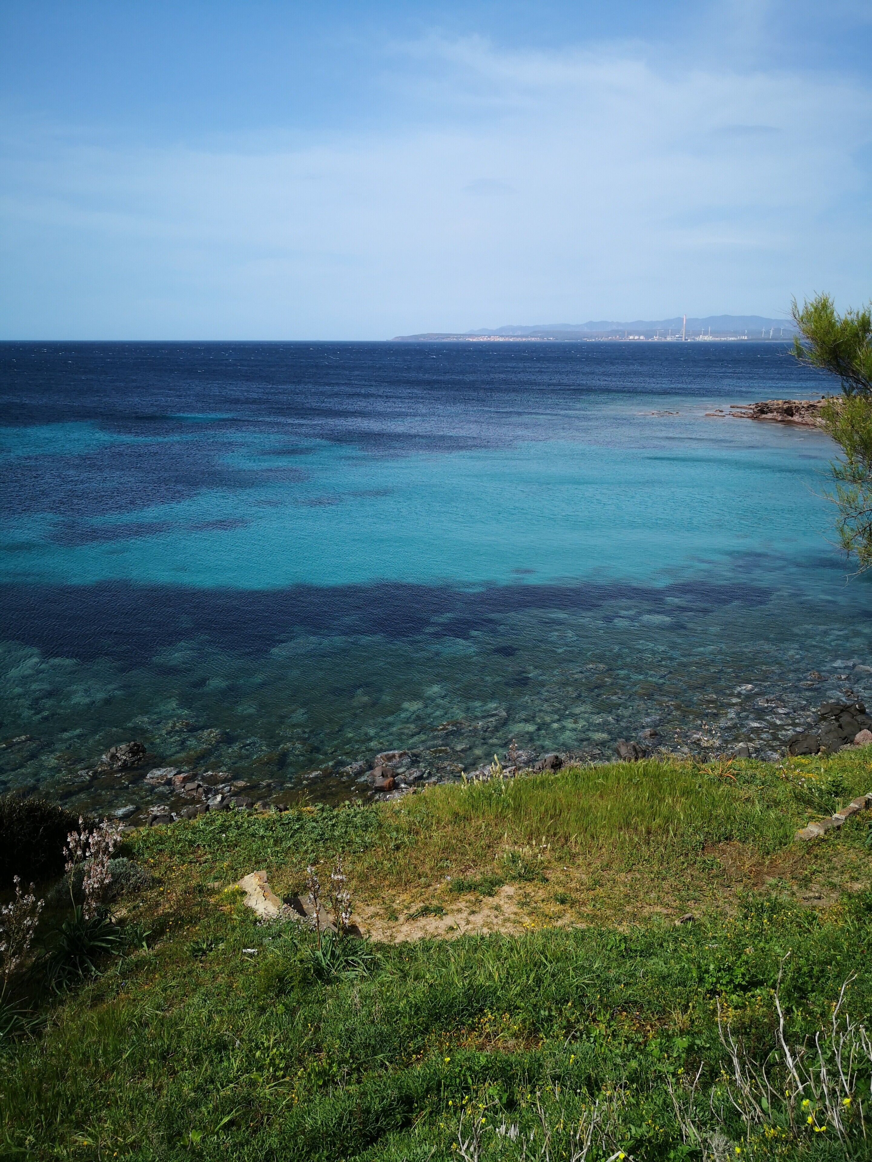 A coastal landscape with clear waters, rocky shoreline, and greenery.