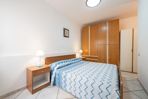 Een slaapkamer met een bed, een houten garderobe, nachtkastjes en een lijst met een afbeelding aan de muur.
