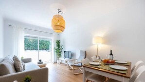 A modern living room with a sofa, a dining table with chairs, a hanging light fixture, and a large window. - Holiday Home 'Casa Cláudia - Cond  Atalaia' with Shared Pool, Private Terrace and Wi-Fi (Lagos)