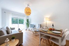 A modern living room with a sofa, a dining table with chairs, a hanging light fixture, and a large window. - Holiday Home 'Casa Cláudia - Cond  Atalaia' with Shared Pool, Private Terrace and Wi-Fi (Lagos)