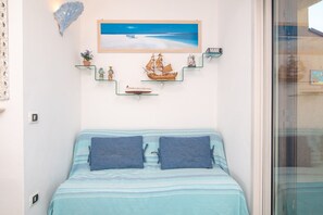 A bedroom with a bed, a painting of a beach scene, and a ship model.
