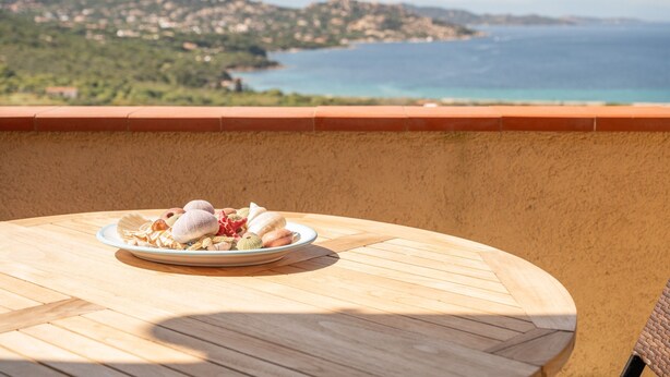 Una mesa redonda de madera con un plato de comida y vistas a un paisaje costero.