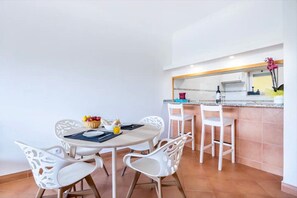 A dining area with a round table and white chairs, a kitchen with a counter and sink, and a tiled floor. - Apartment 'Casa Cláudia - Cond Do Mar' with Sea View, Shared Pool and Wi-Fi (Lagos)