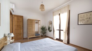 A bedroom with a bed, a wooden wardrobe, a mirror, a hanging lamp, and a window with curtains. - Apartment 'Flat Arcipelago' with Shared Pool, Wi-Fi and Air Conditioning (Palau)